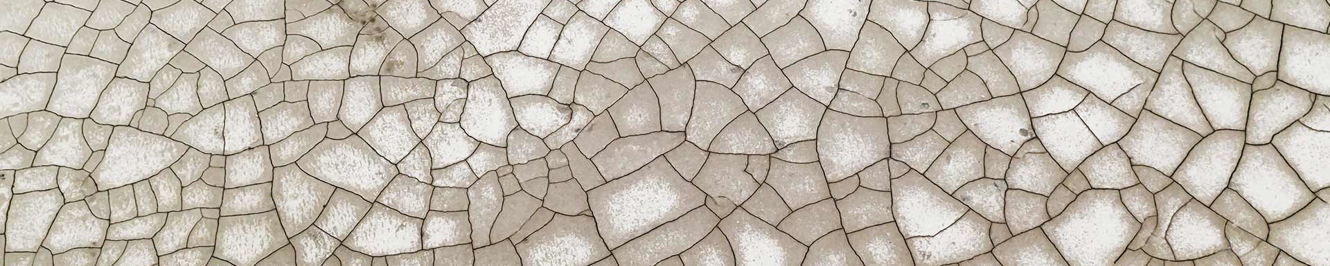 Mann steht auf rissigem, ausgetrocknetem Boden, symbolisiert Dürre und Herausforderungen der Wasserknappheit.