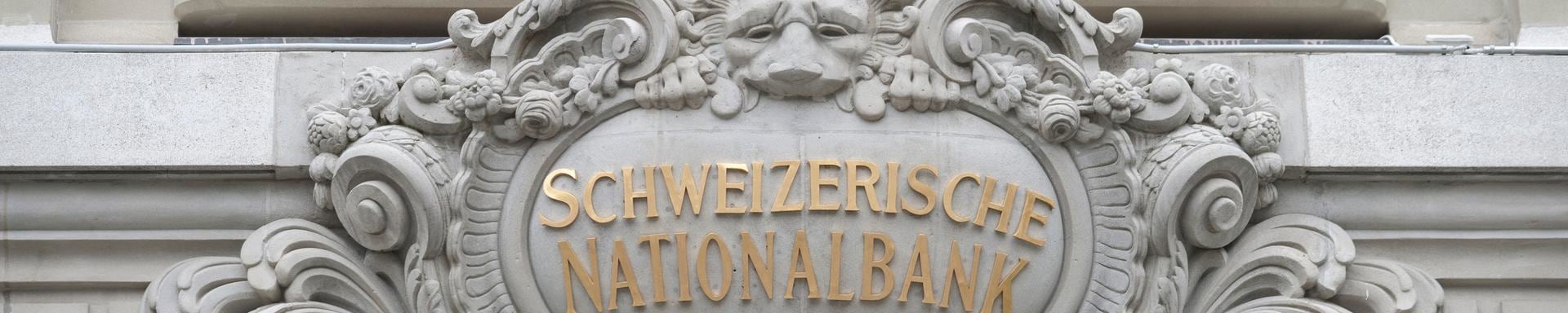 "SCHWEIZERISCHE NATIONALBANK" in goldenen Buchstaben über einem verzierten Steinbogen mit einem dekorativen Ornament.