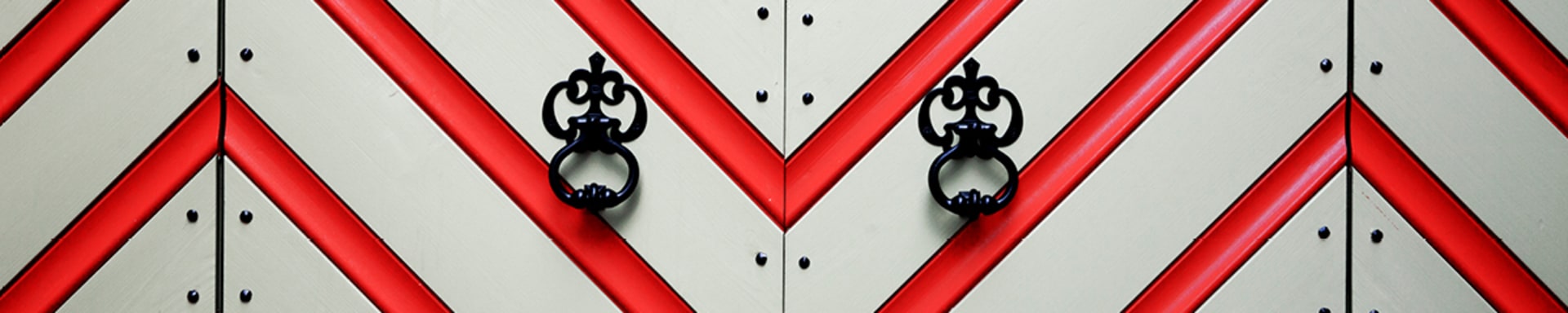 Close-up of a medieval gate. It is painted in a red and white zigzag pattern and decorated with nails.