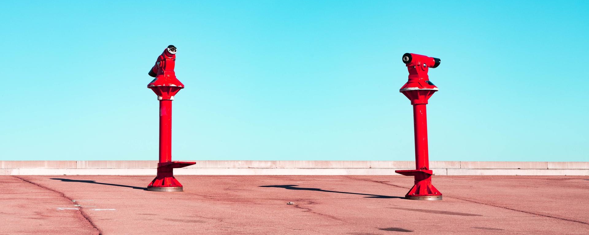 Two red telescopes pointing towards the sky, symbolizing exploration and the pursuit of knowledge in finance and investment.