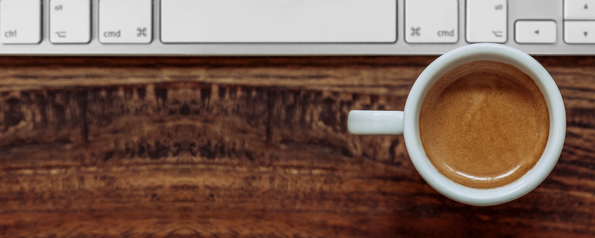 Tastatur mit Kaffee auf einem Holztisch symbolisiert einen Termin mit Vontobel in Ihrer Nähe.
