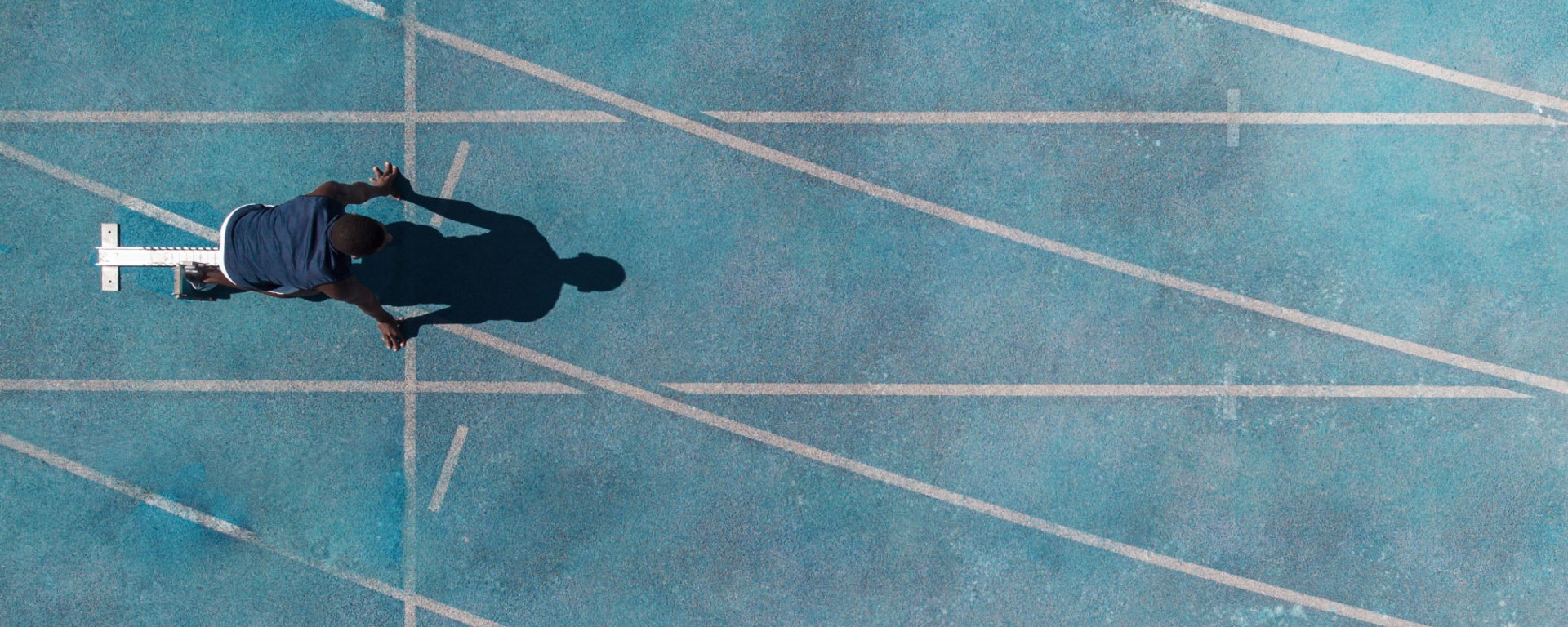 Ein Bild aus der Vogelperspektive von oben auf einen Sportler auf einer blauen Laufbahn der sich vorbereitet auf einen Sprint