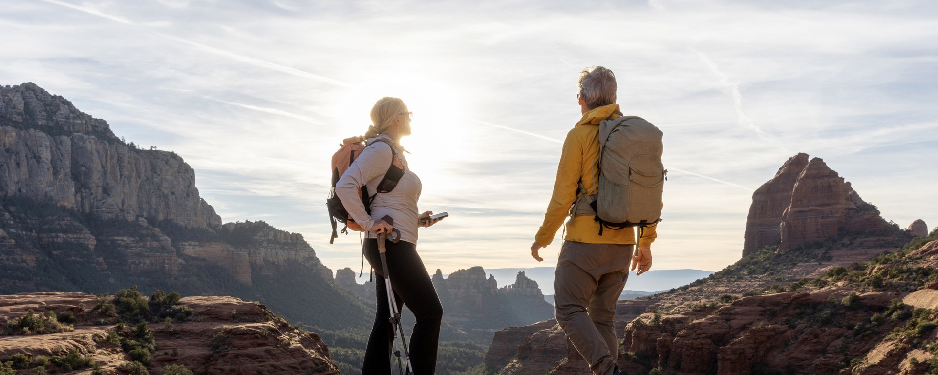 Ein älterer Mann und eine ältere Frau in Wanderkleidung stehen auf einem Felsvorsprung und geniessen die Aussicht. Sinnbild für das Planen der eigenen Pensionierung mit einem ganzheitlichen Vermögenskonzept.