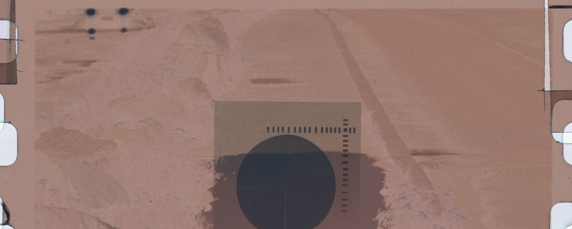 Abstract filmstrip photograph with brown-beige textures, black circle and square, and calibration markings