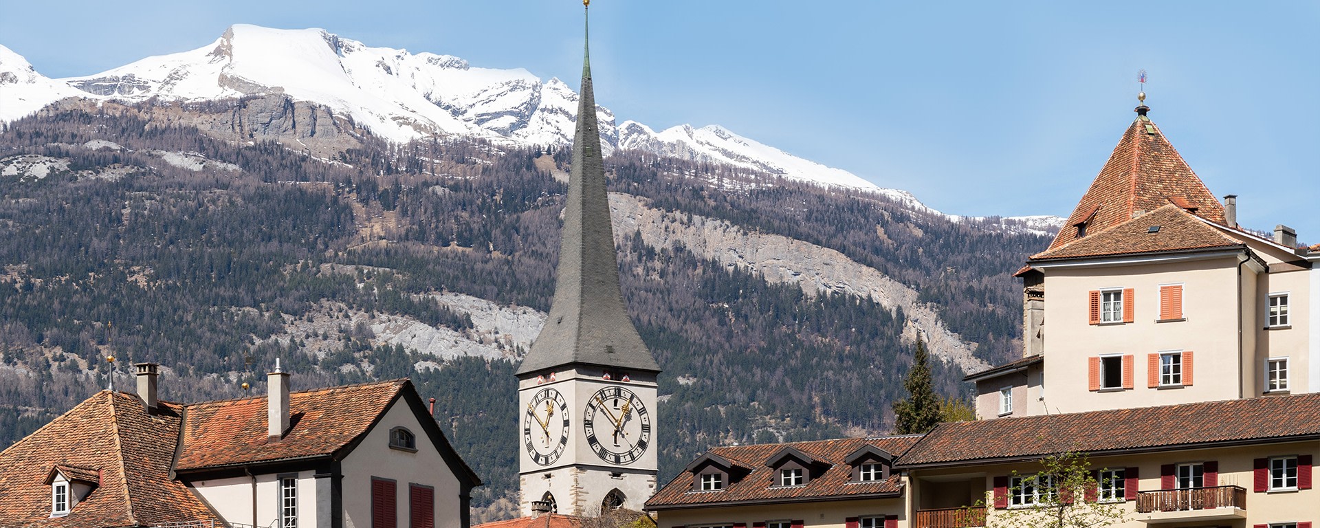 La città di Coira, con il campanile della chiesa in primo piano e le montagne innevate sullo sfondo.