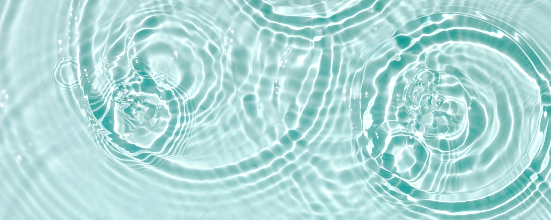 Abstract close-up of turquoise water with concentric ripples and light reflections