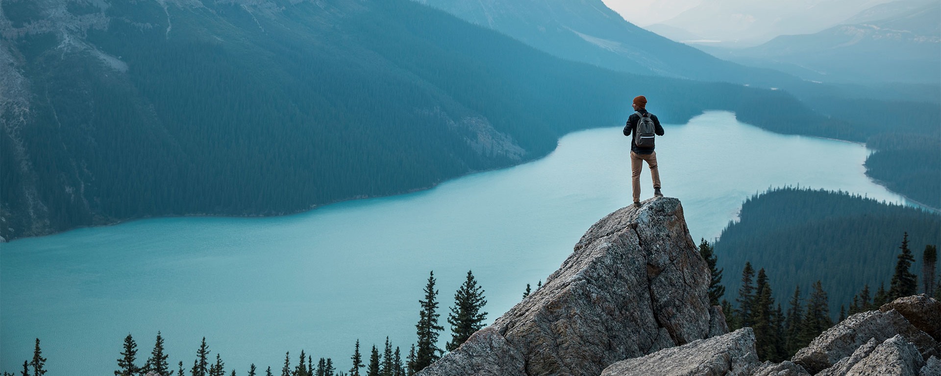 A young hiker stands on a rocky outcrop and looks at the mountain panorama.