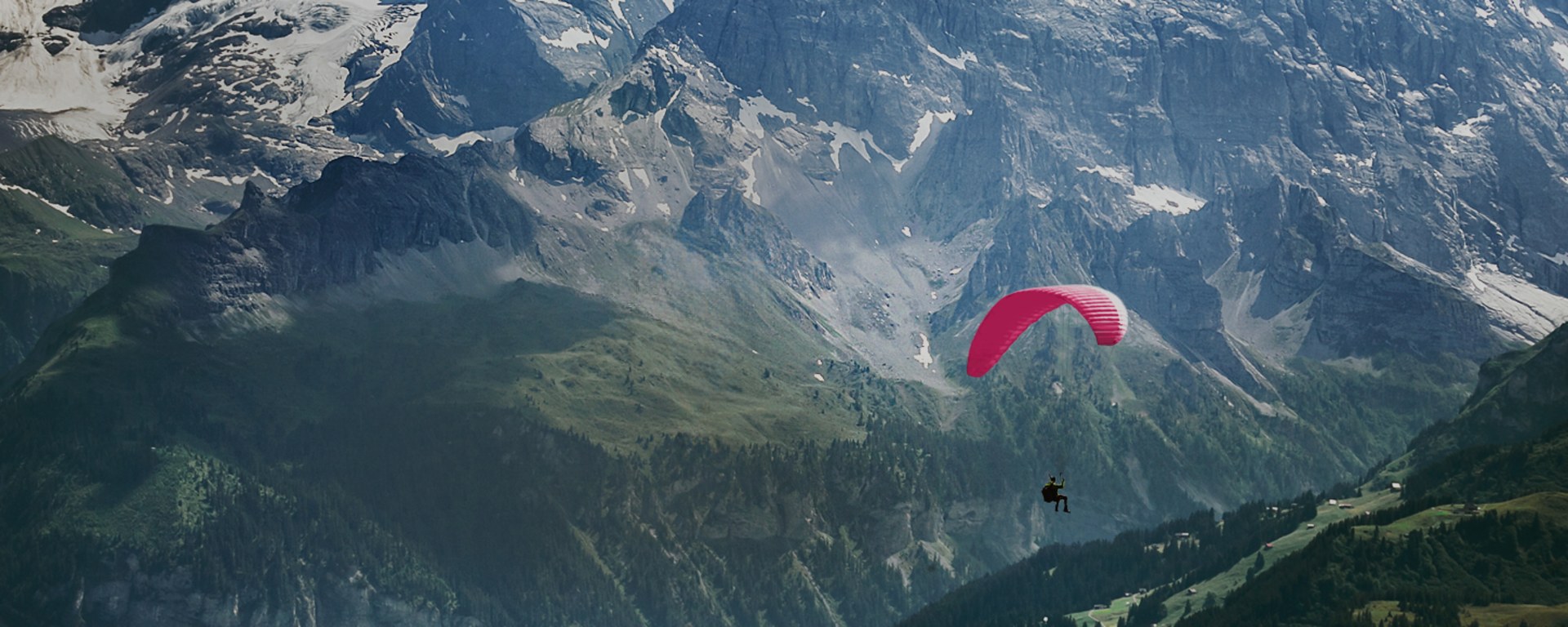 A paraglider is flying through the Swiss mountain landscape.