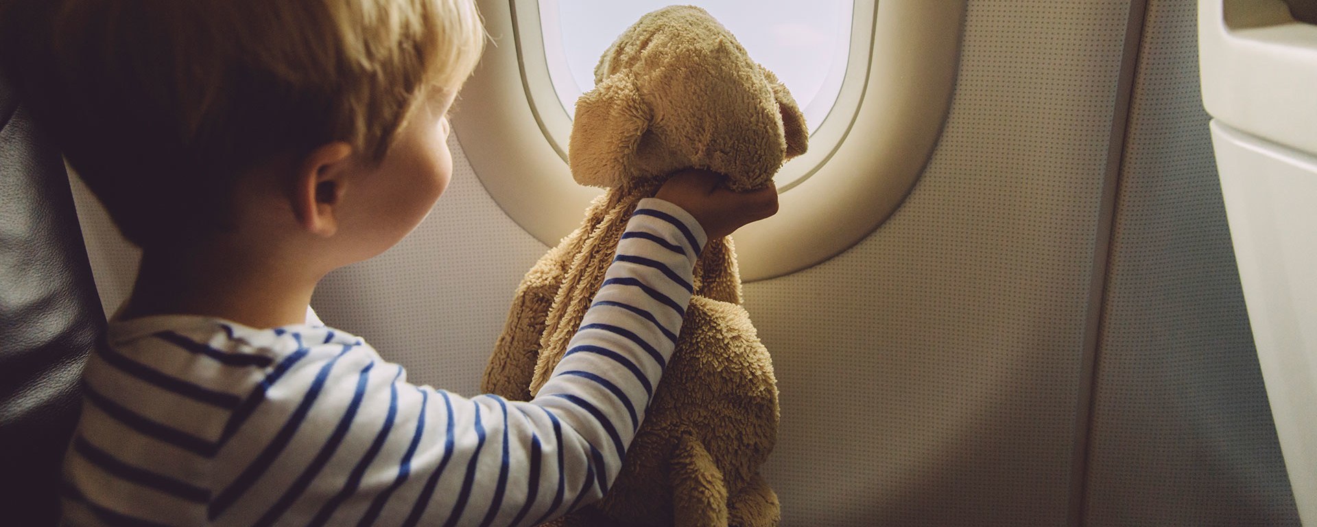 Child in an airplane looking out of the window with his stuffed animal