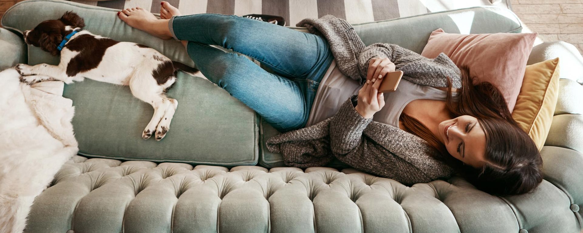 E-Banking bei Vontobel - Glückliche Frau liegt mit ihrem Hund auf einem Sofa und hat ihr Handy in der Hand