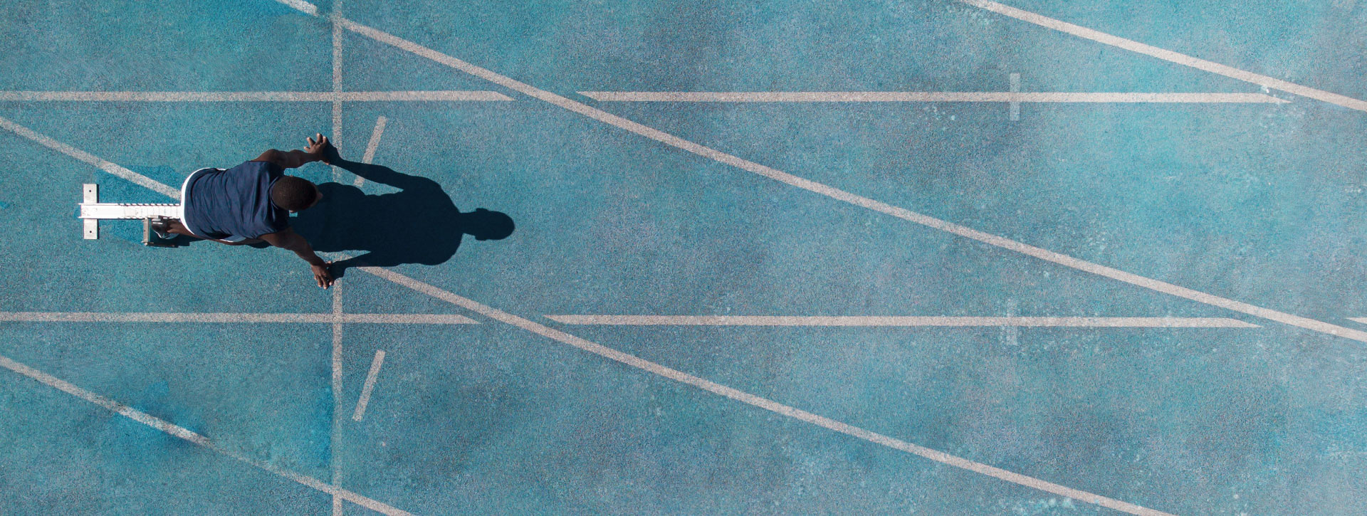 A bird's eye view of an athlete on a blue running track preparing for a sprint