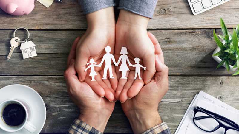 Vier Hände, die auf einem Tisch sind und eine ausgeschnittene Familie aus Papier halten