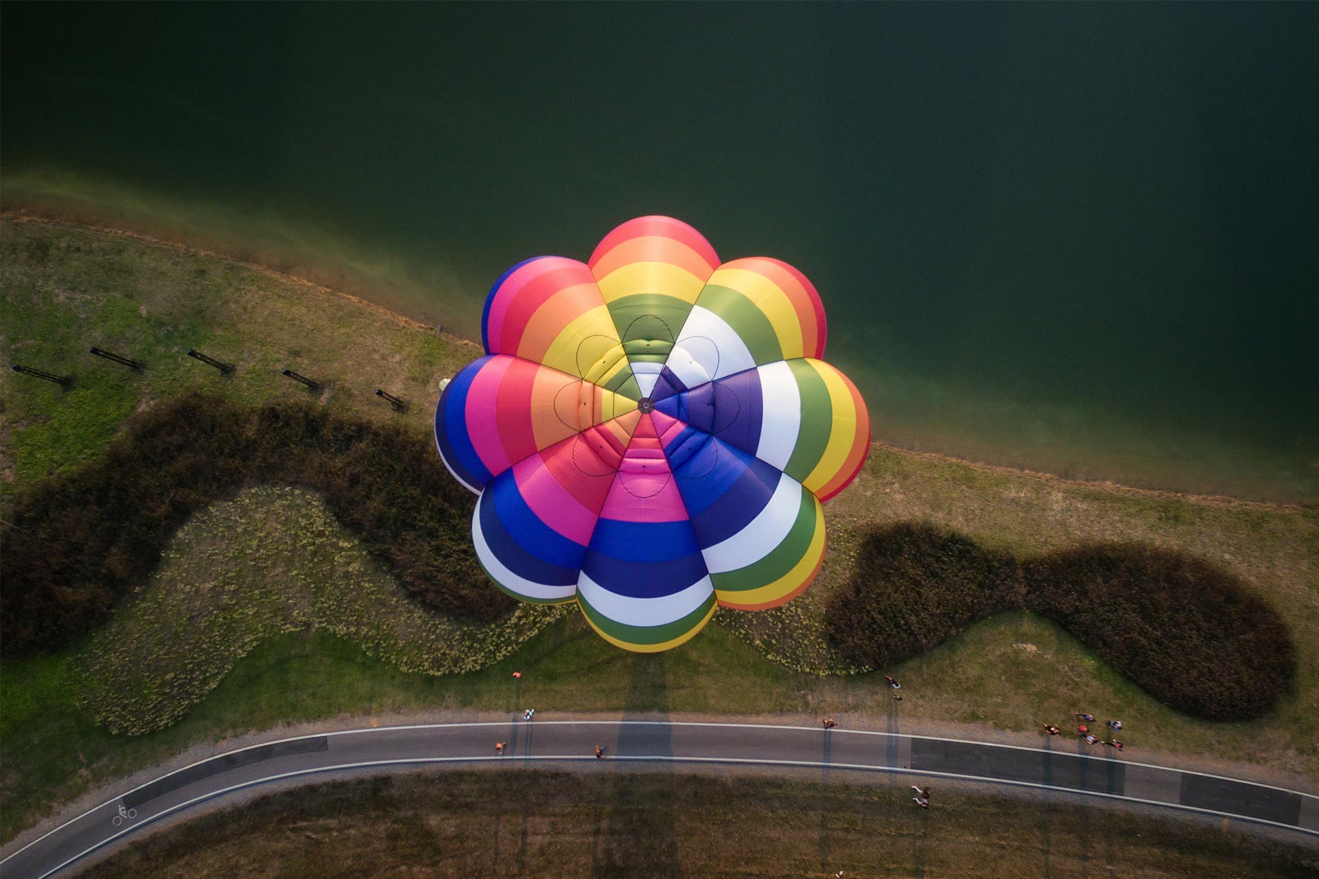 Ein farbiger Heissluftballon fliegt über eine Wiese - aus der Vogelperspektive.