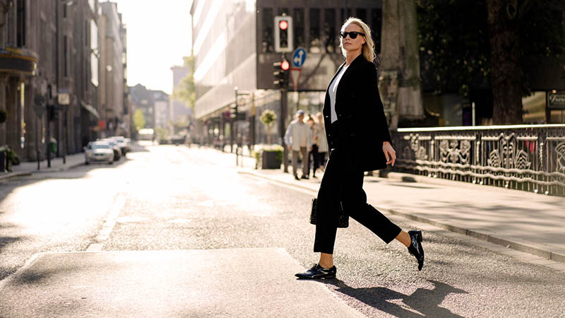 A woman in a black suit and sunglasses confidently crossing a street.