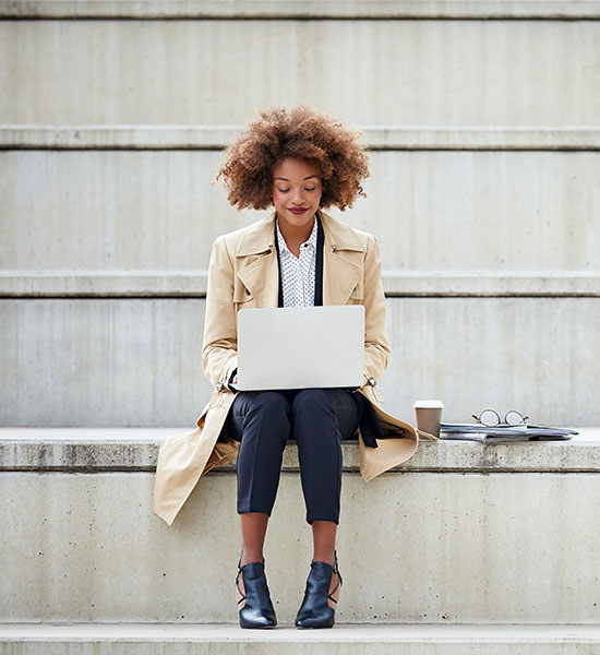 Young woman sitting on a concrete staircase and working with a laptop on her lap.
