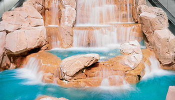 Indoor waterfall cascading down a wall, surrounded by lush greenery, creating a serene atmosphere.