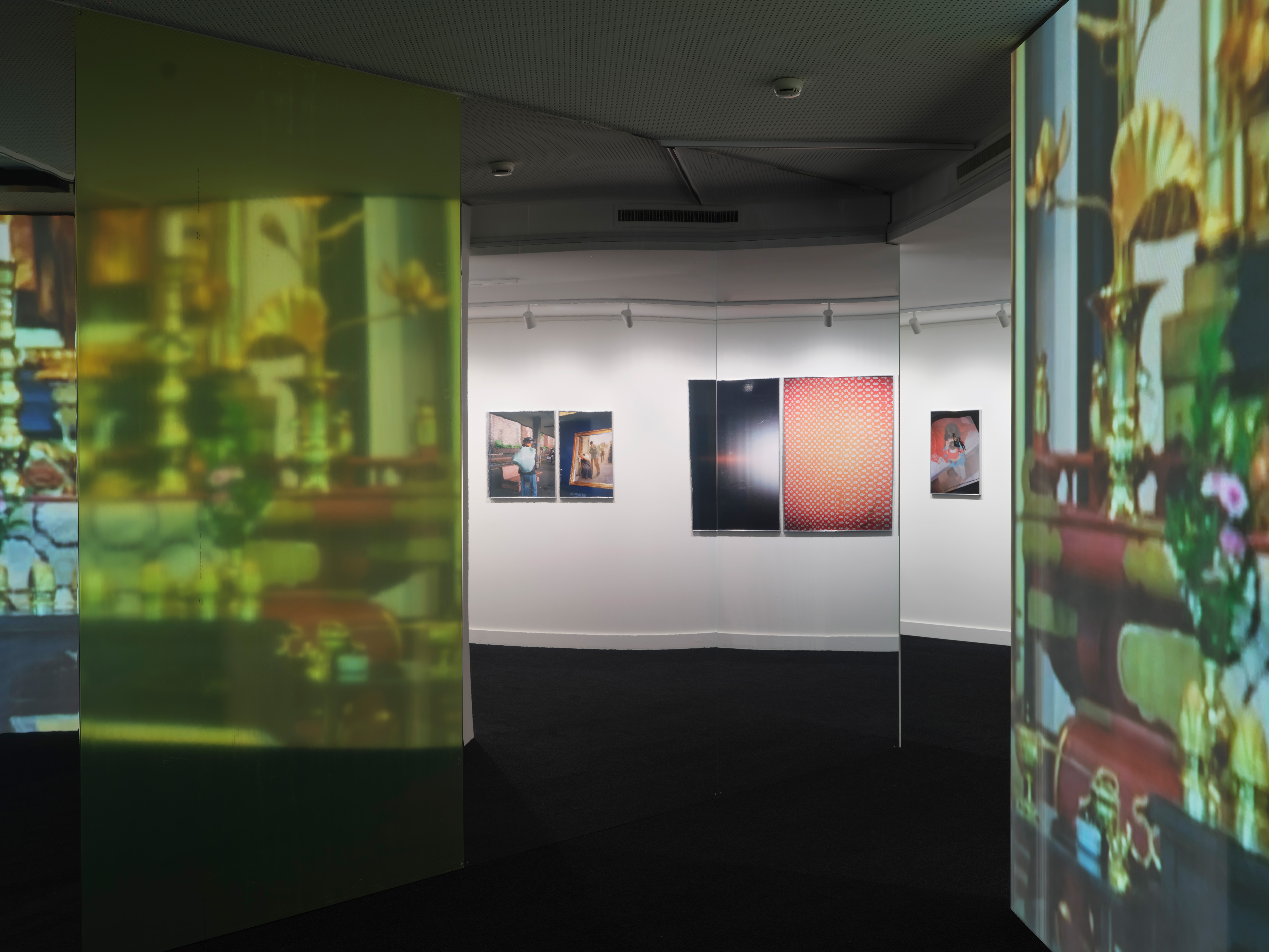Ausstellungsraum mit halbtransparenten Projektionsflächen, die unscharfe Innenraumdarstellungen zeigen, und gegenüber hängenden Fotografien an einer weissen Wand