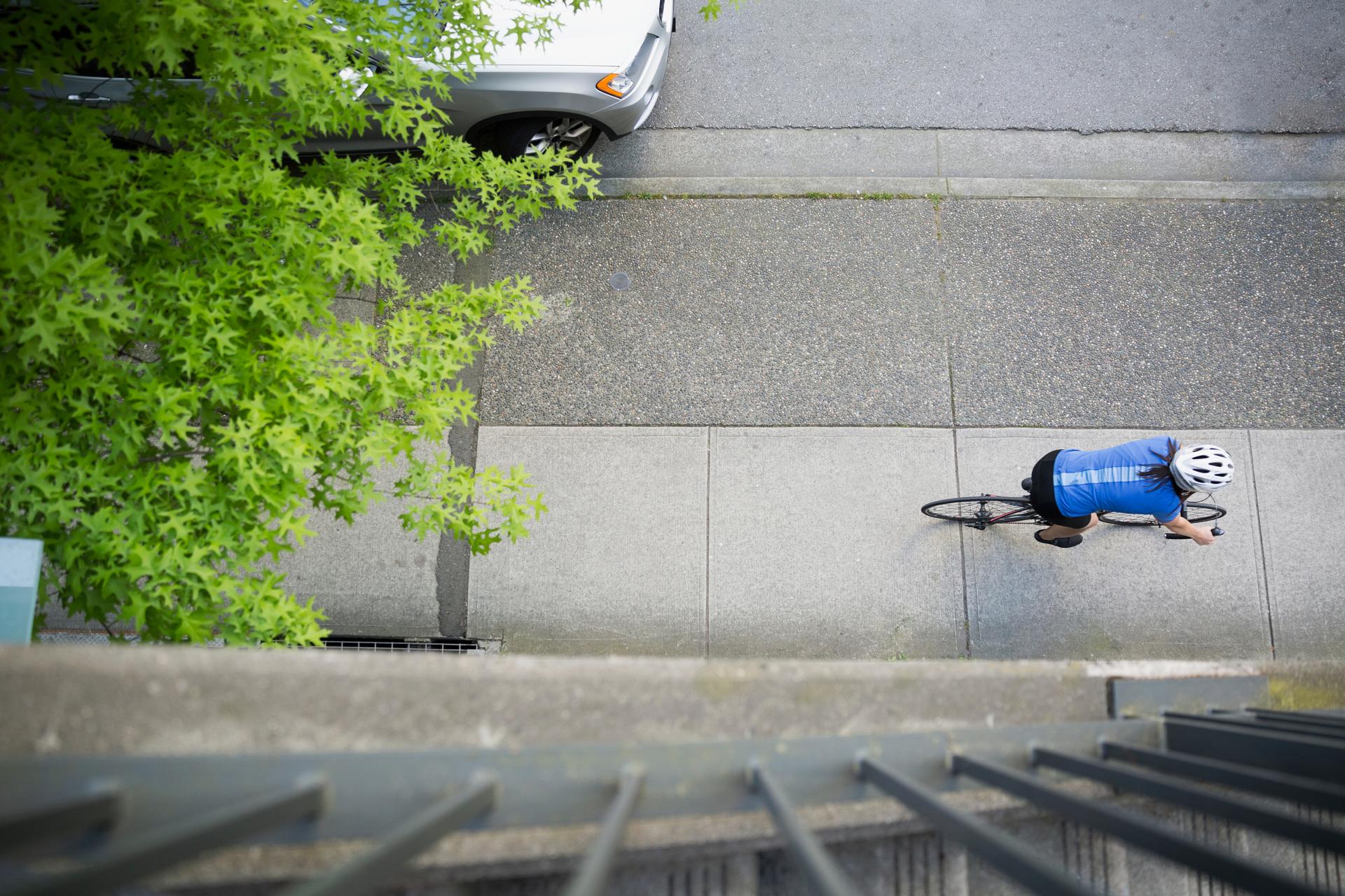 Bird's eye view from a balcony, down onto a woman riding a bicycle.