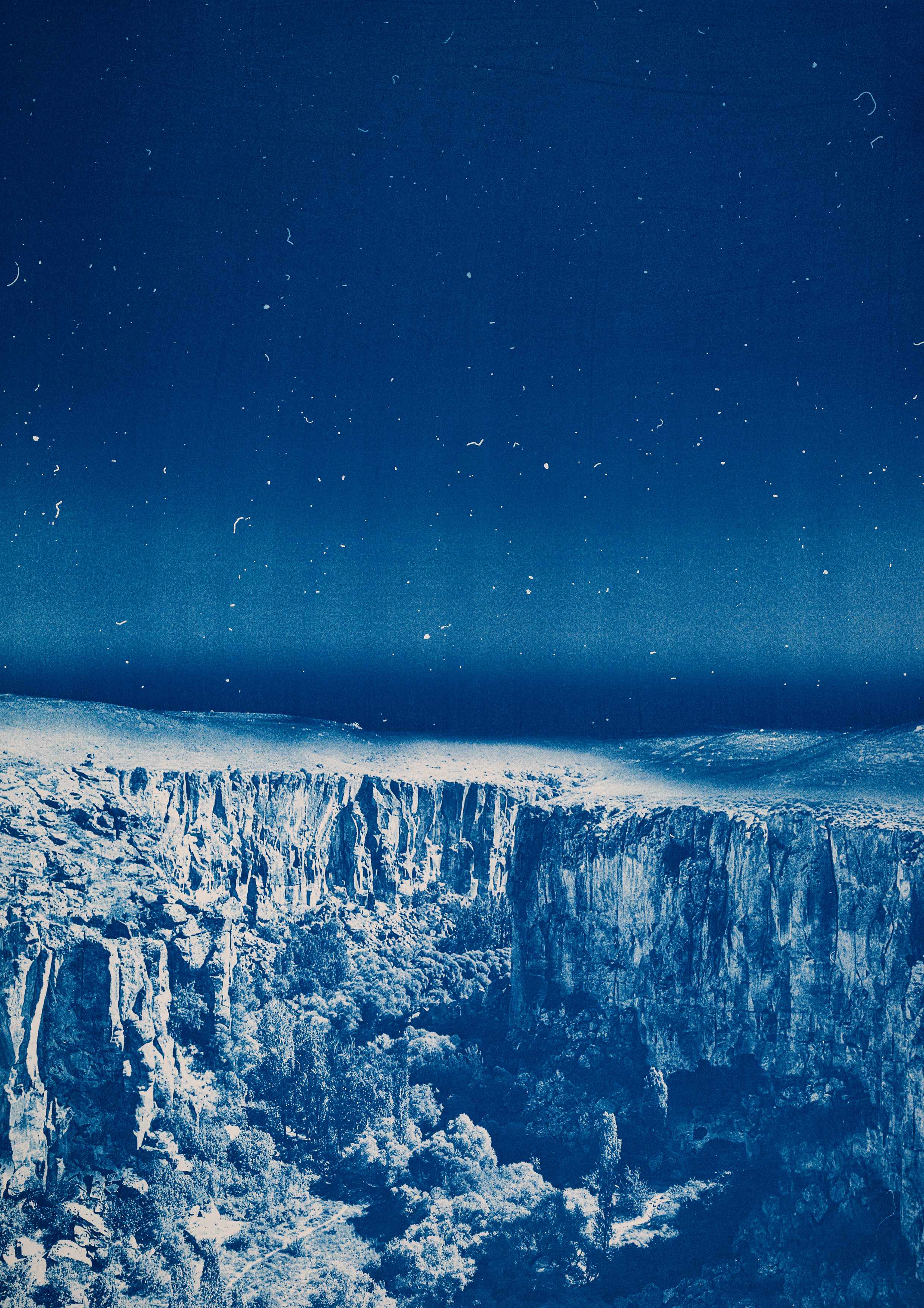 Blue-toned image of steep rocky cliffs and rugged landscape under a dark sky, with textured terrain extending across the horizon.