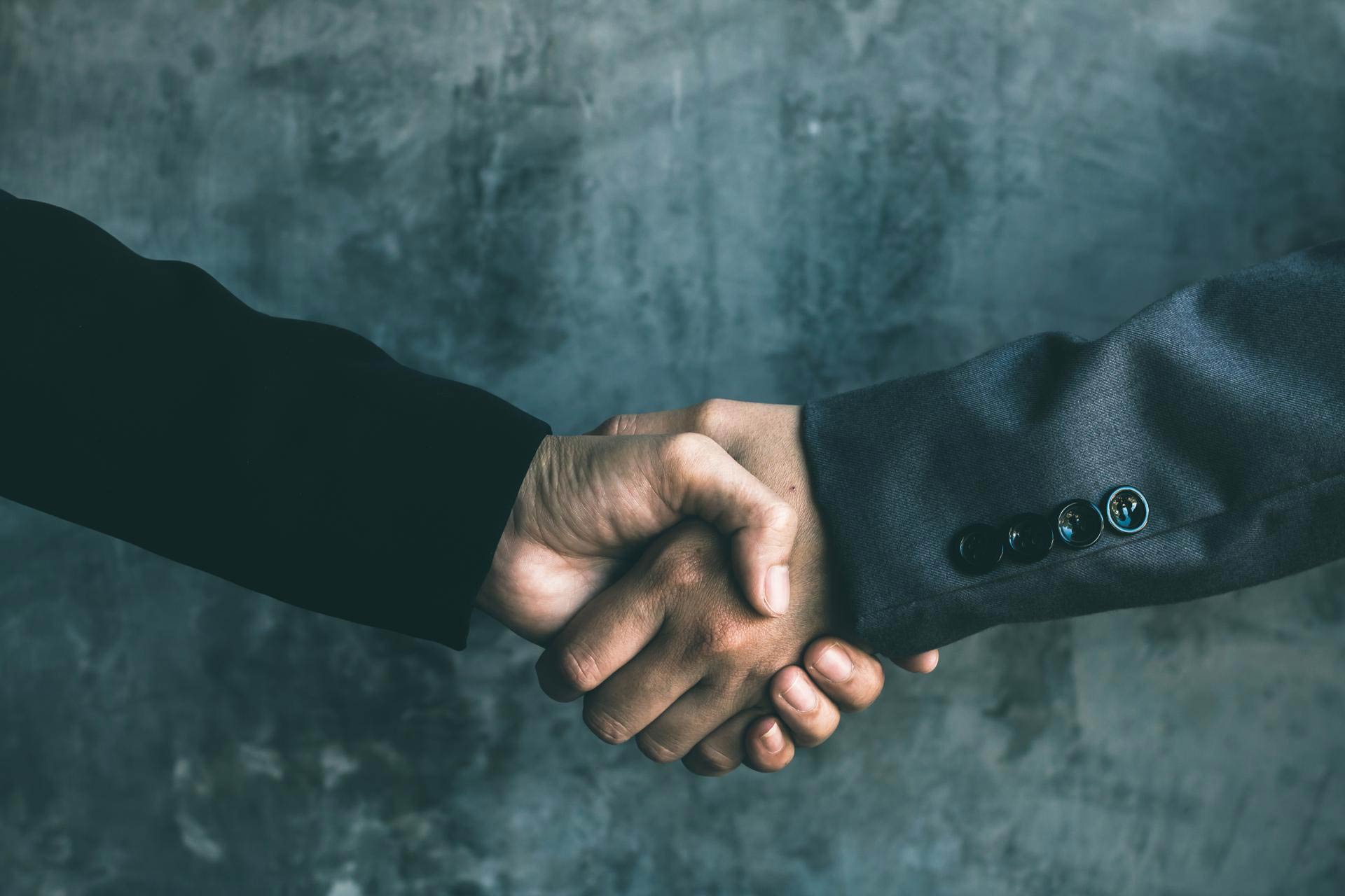 Zwei Geschäftsmänner im Anzug schütteln sich die Hände im Rahmen einer geschäftlichen Beziehung