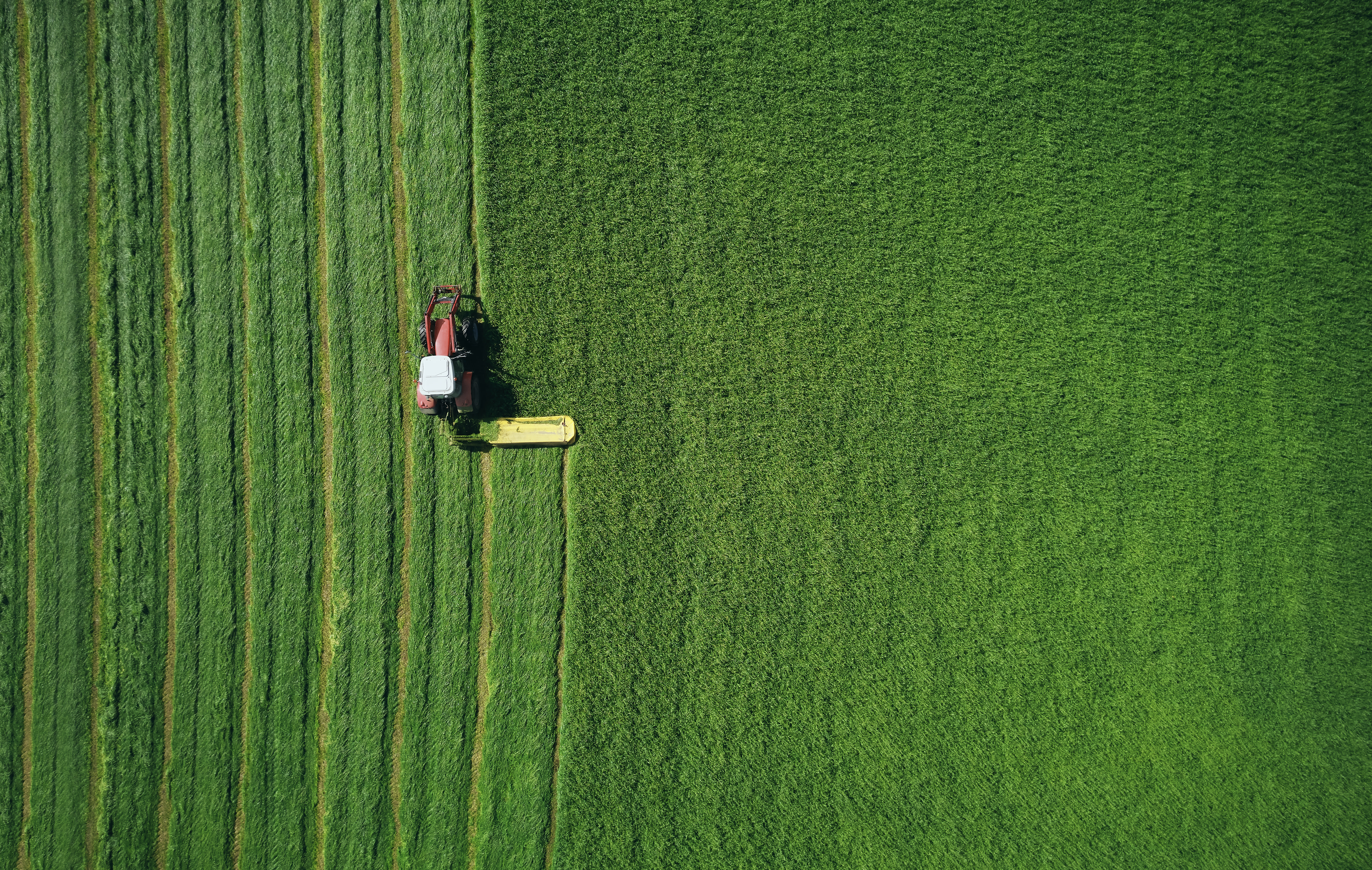 Aerial view of a tractor mowing green agricultural fields, illustrating modern farming practices, productivity, and sustainable land use