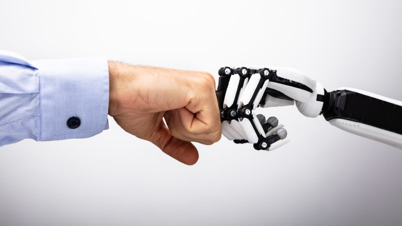 Eine menschliche Hand und eine robotische Hand halten ihre Fäuste zusammen.