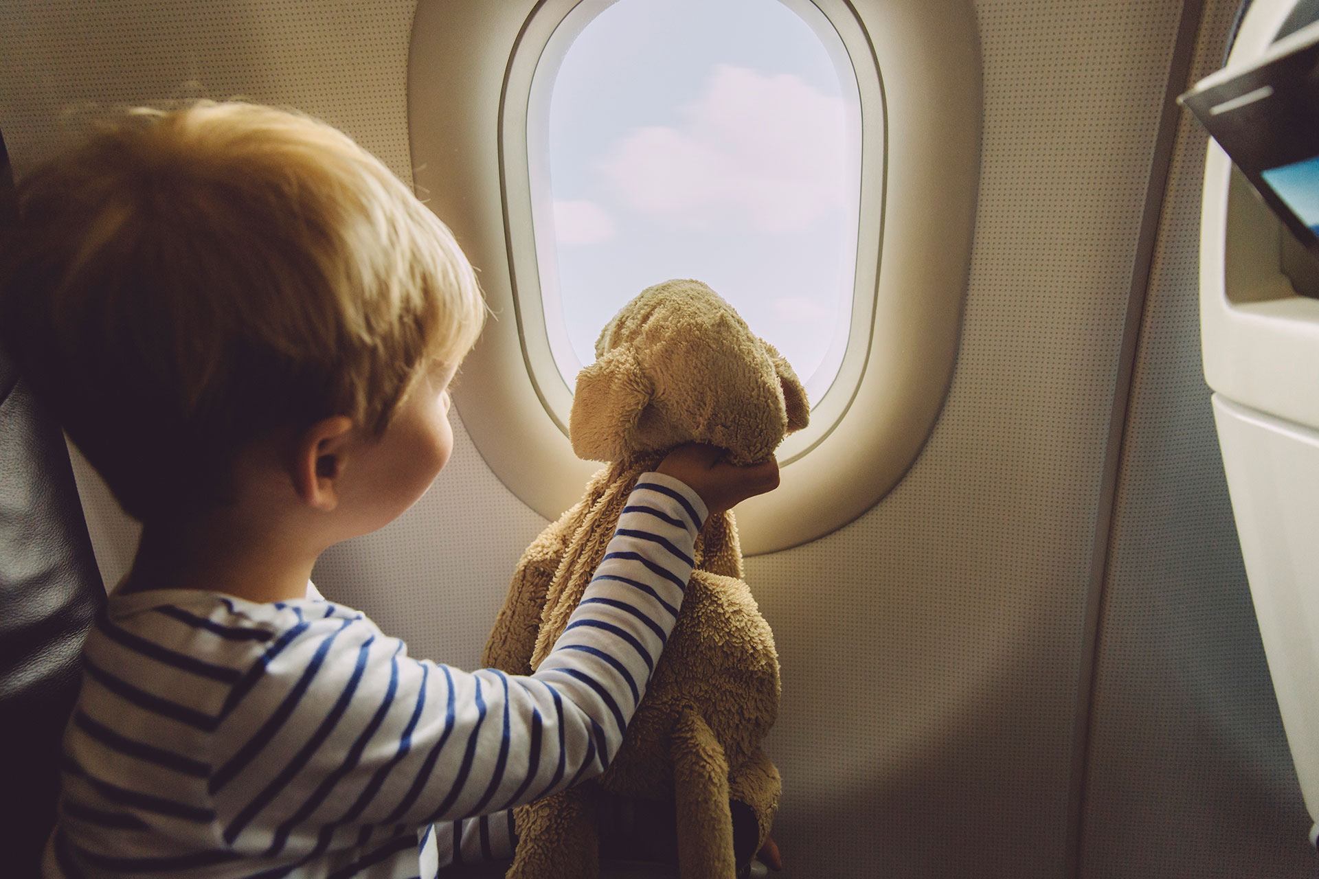 Child in an airplane looking out of the window with his stuffed animal