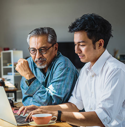 A young man shows an older man something on his laptop