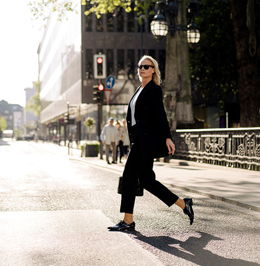 A business woman walking confidently across a street in a big city.