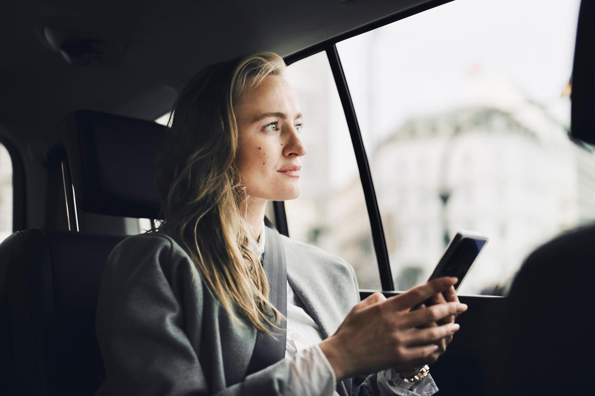 Eine Frau sitzt in einem fahrenden Auto und schaut auf ihr Smartphone, während sie mit der Volt-App Investitionen tätigt.