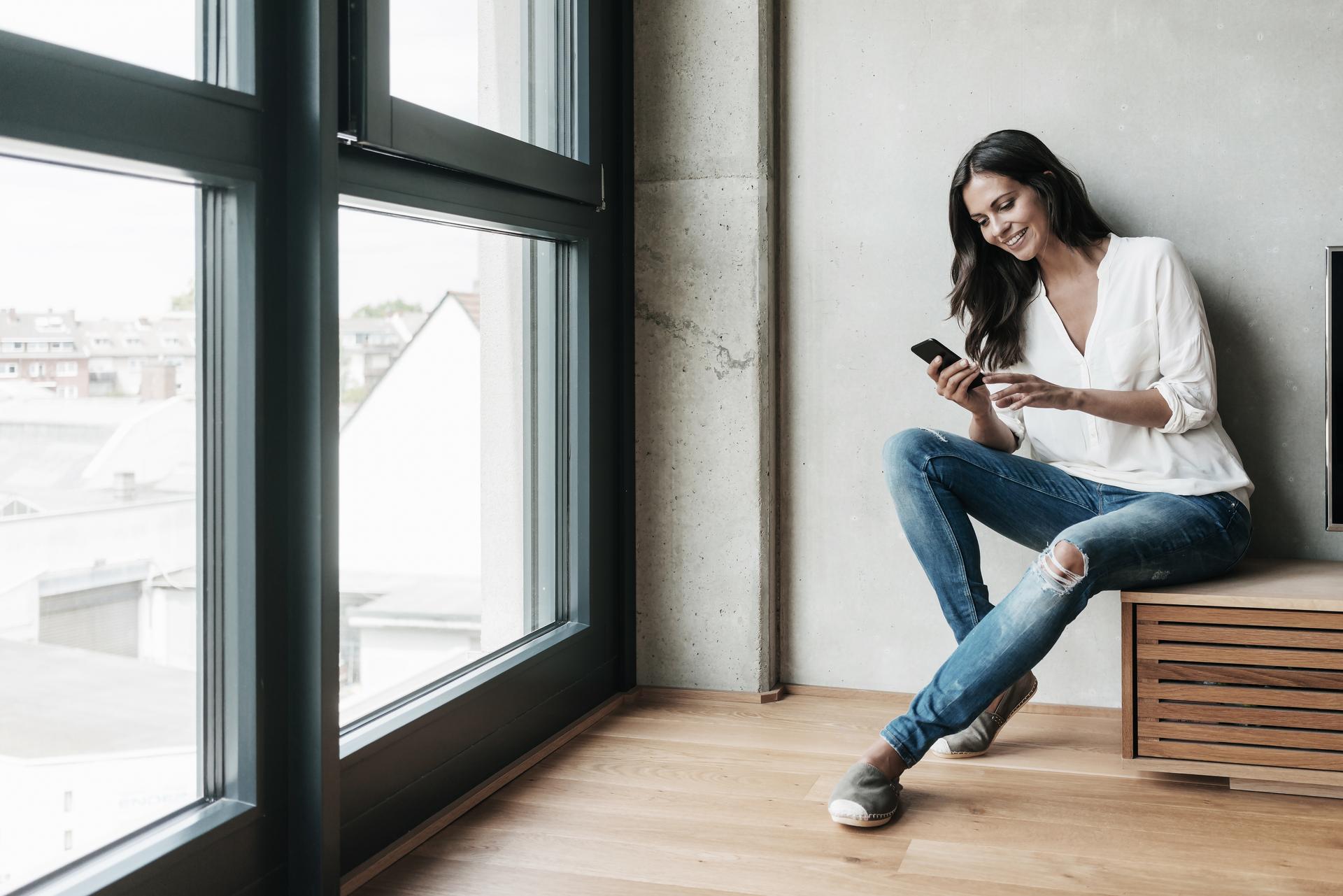 Eine junge Frau sitzt in ihrem Wohnzimmer und schaut auf ihr Smartphone, während sie die volt App benutzt.