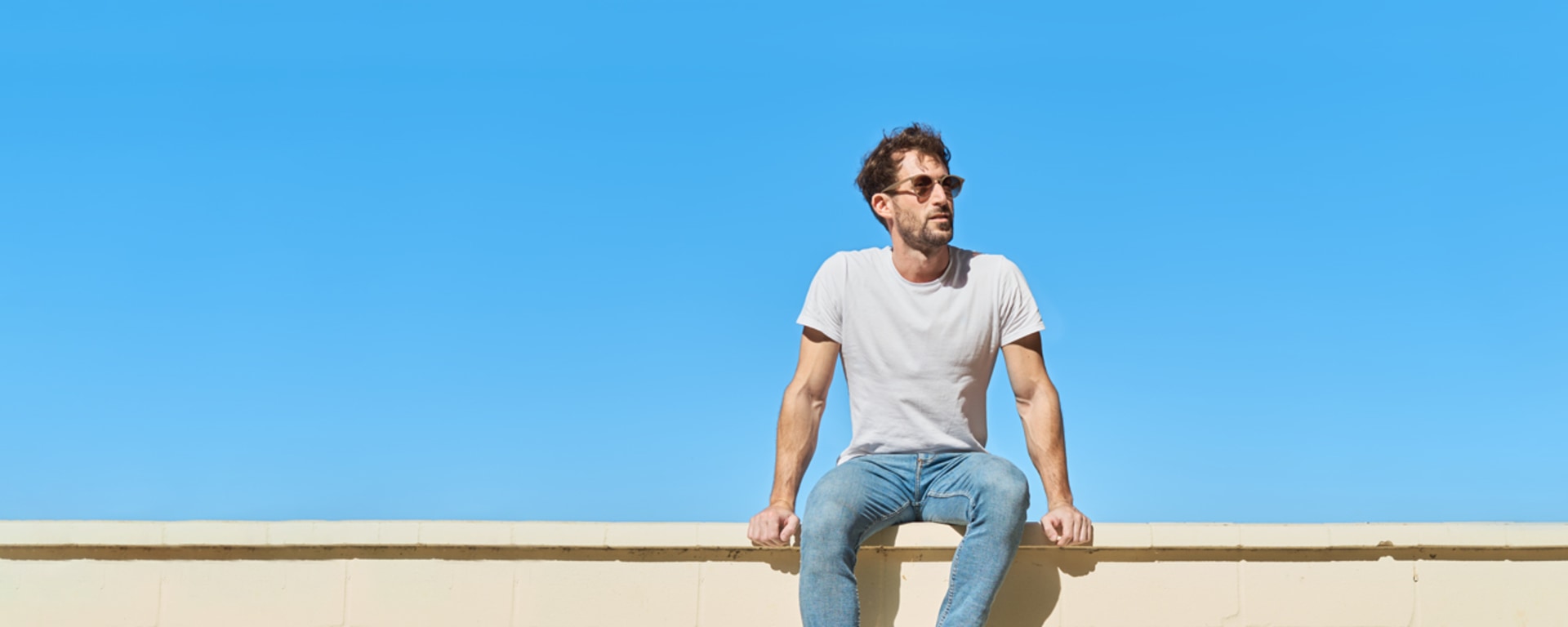 Ein junger Mann mit Sonnenbrille sitzt auf einer Mauer.