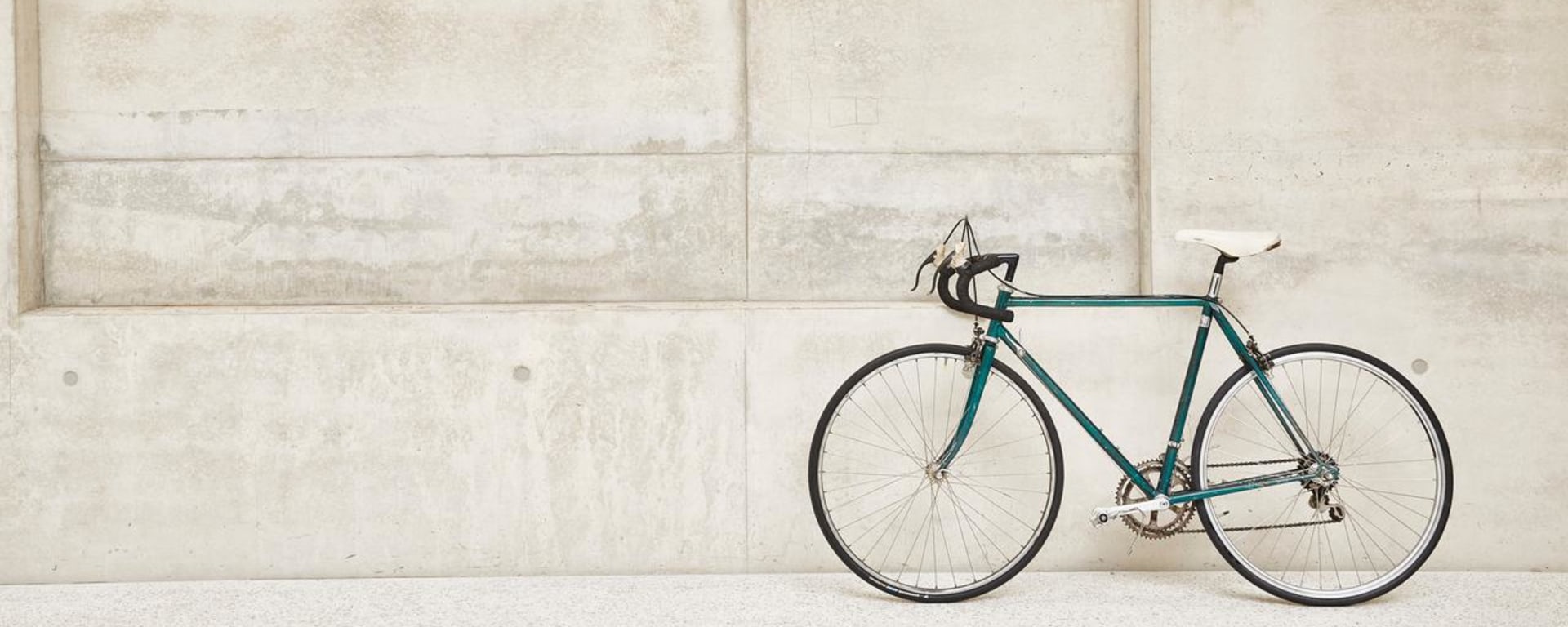 A green racing bike leaning against a concrete wall