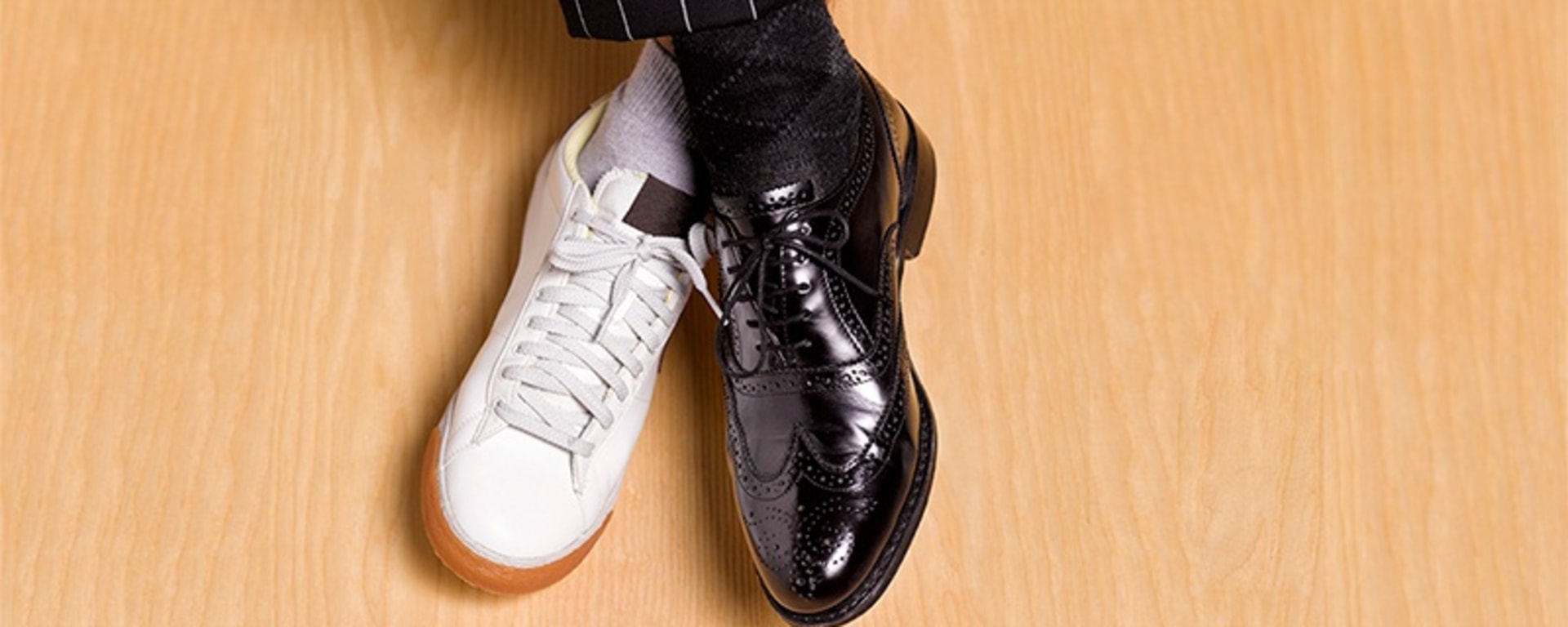 Ein Mann, der schwarze Anzugschuhe und weiße Turnschuhe trägt und damit eine Mischung aus formellem und legerem Schuhwerk präsentiert.