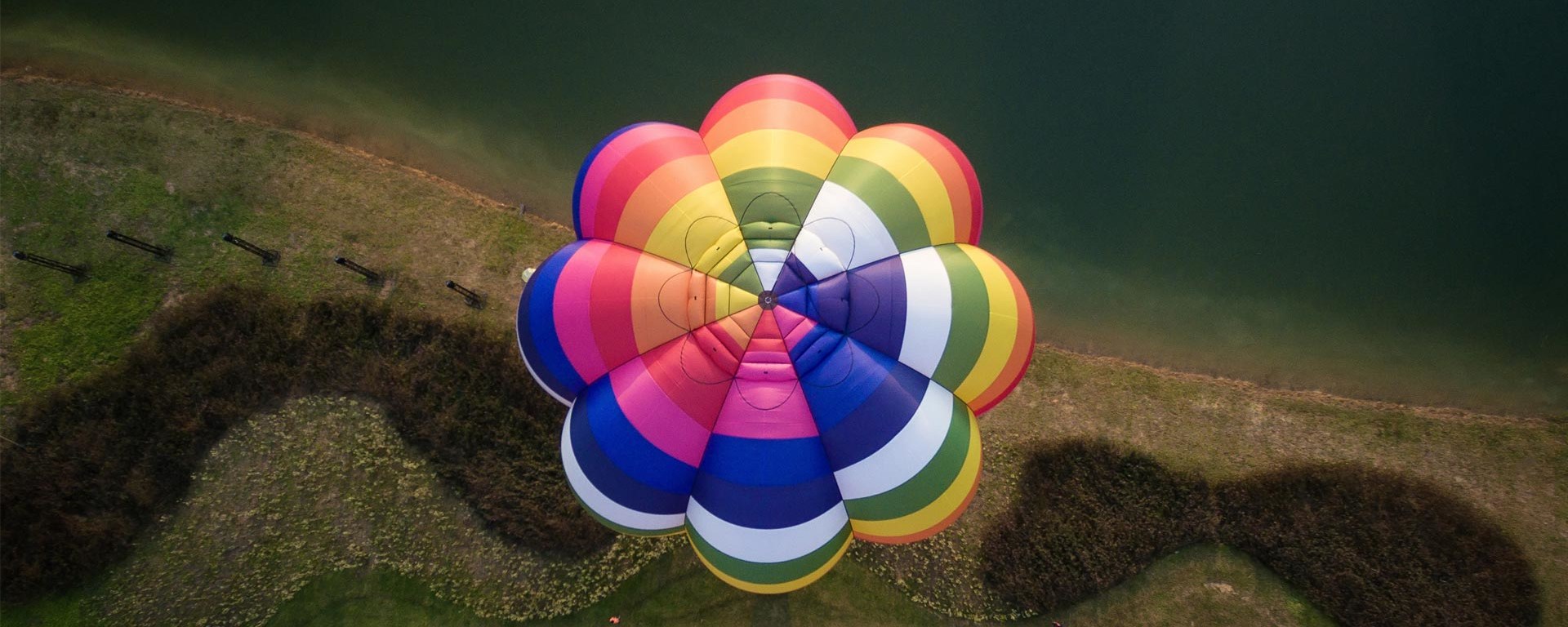 Ein farbiger Heissluftballon fliegt über eine Wiese - aus der Vogelperspektive.