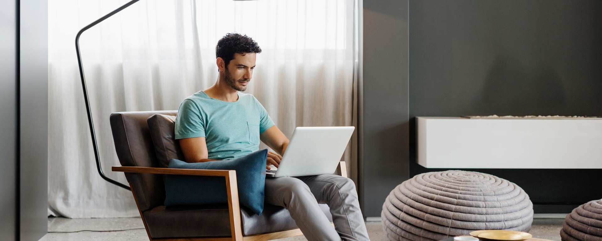 Un homme avec un T-shirt bleu est assis chez lui devant son ordinateur portable et se connecte à son service de banque en ligne.
