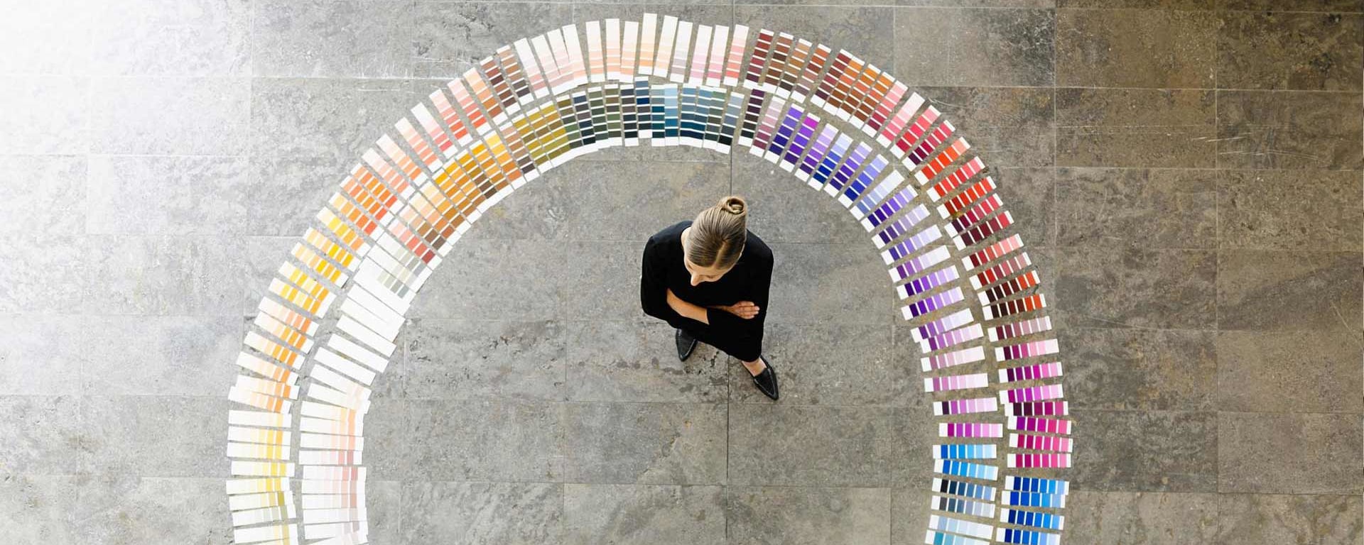 A woman stands in front of a circle of different colors and thinks