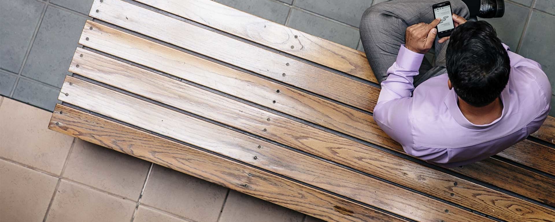 Un hombre está sentado en un banco de madera y mira una publicación en su teléfono inteligente.