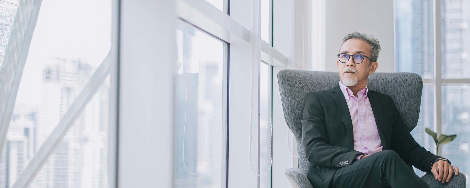 Ein asiatischer Geschäftsmann sitzt in einem Bürosessel und blickt aus dem Fenster
