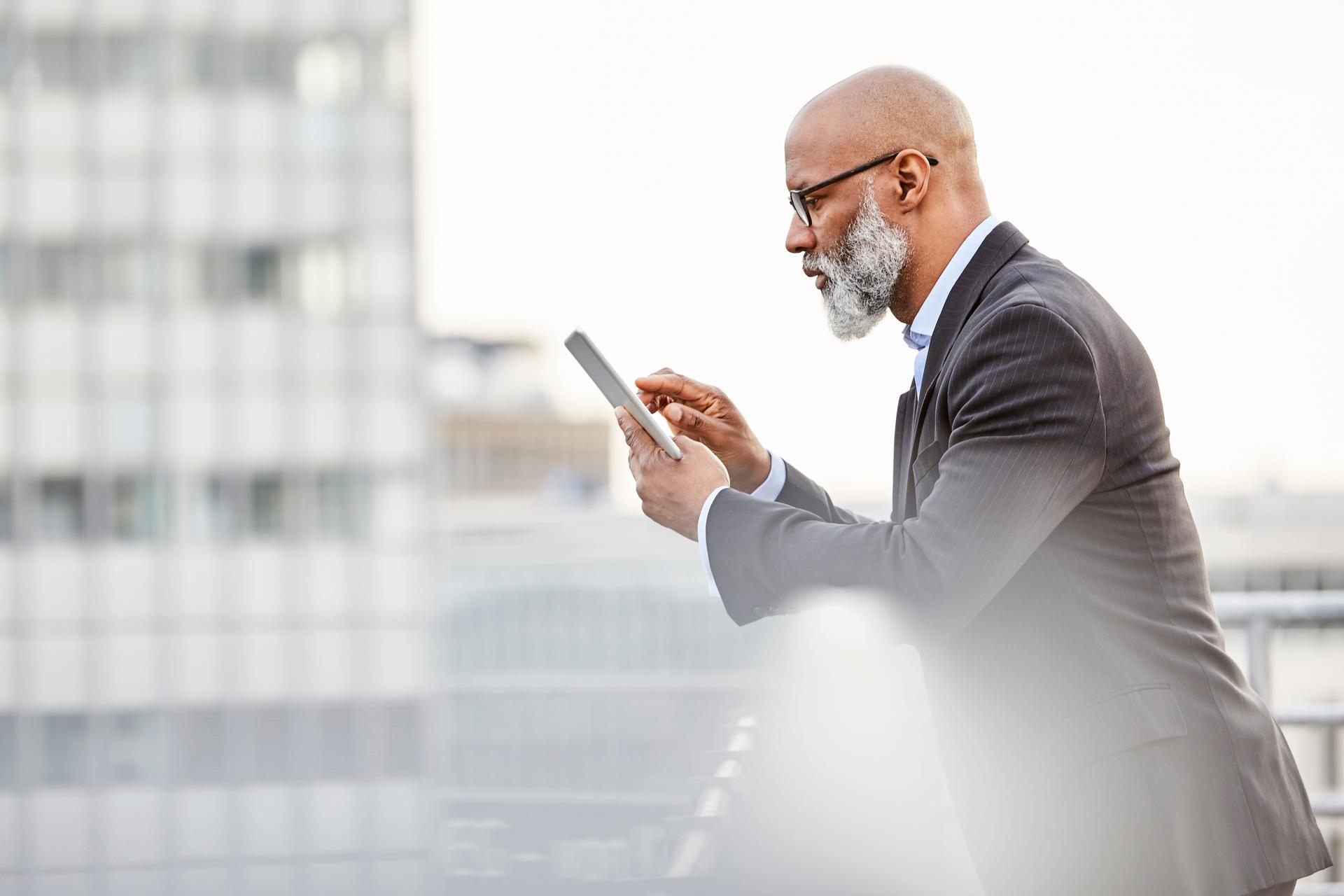Un uomo d'affari si appoggia a una ringhiera e guarda il suo smartphone