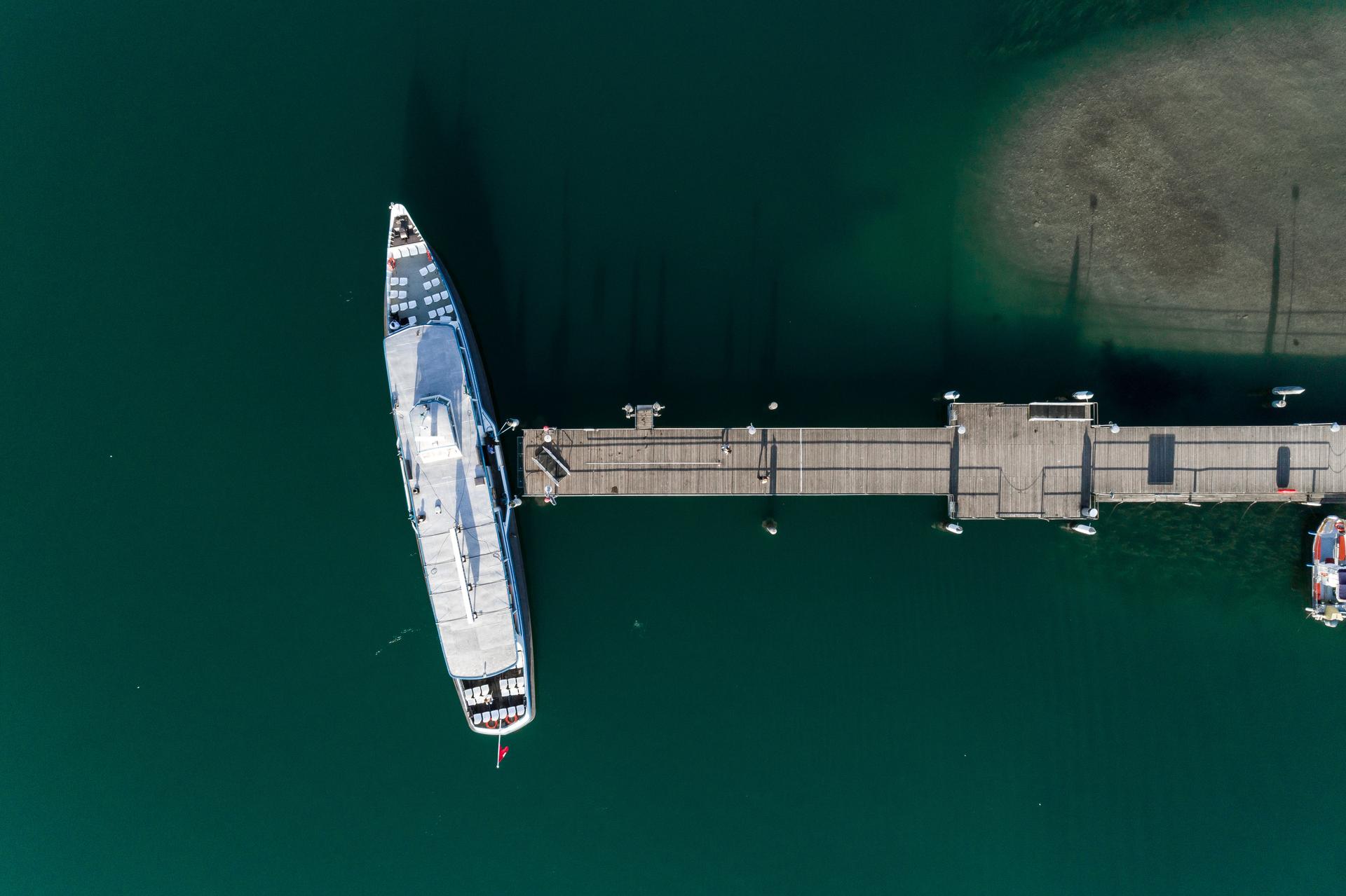 Luftaufnahme eines Schiffs, das an einem Pier angelegt ist, umgeben von tiefgrünem Wasser.