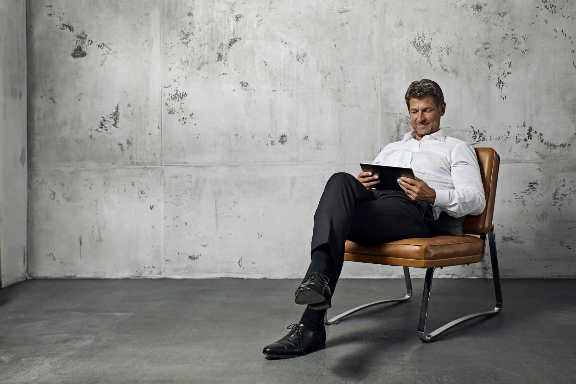 Ein Mann sitzt auf einem ledernen Stuhl und schaut auf sein Tablet