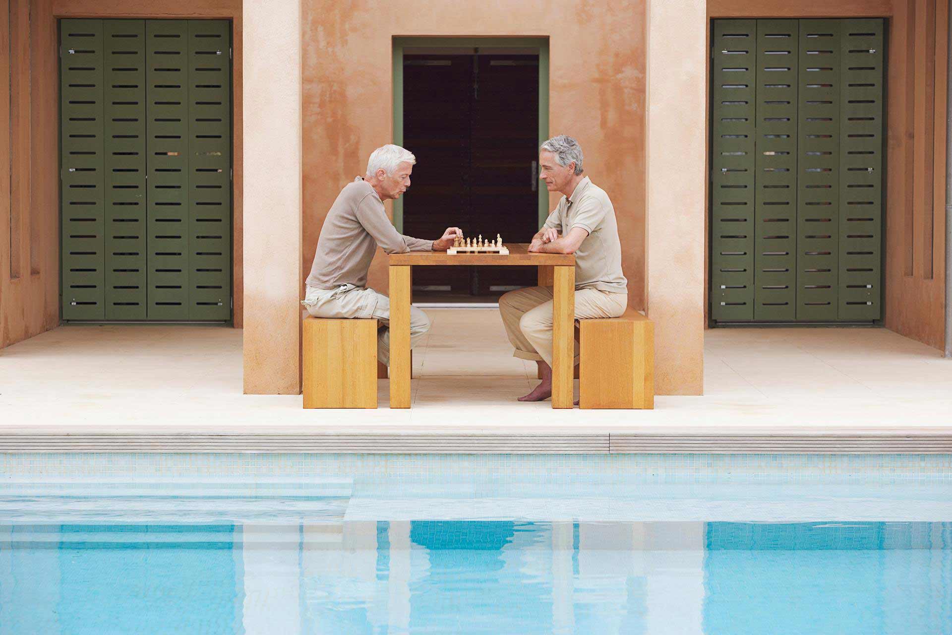Two men sit by a pool and play a game of chess