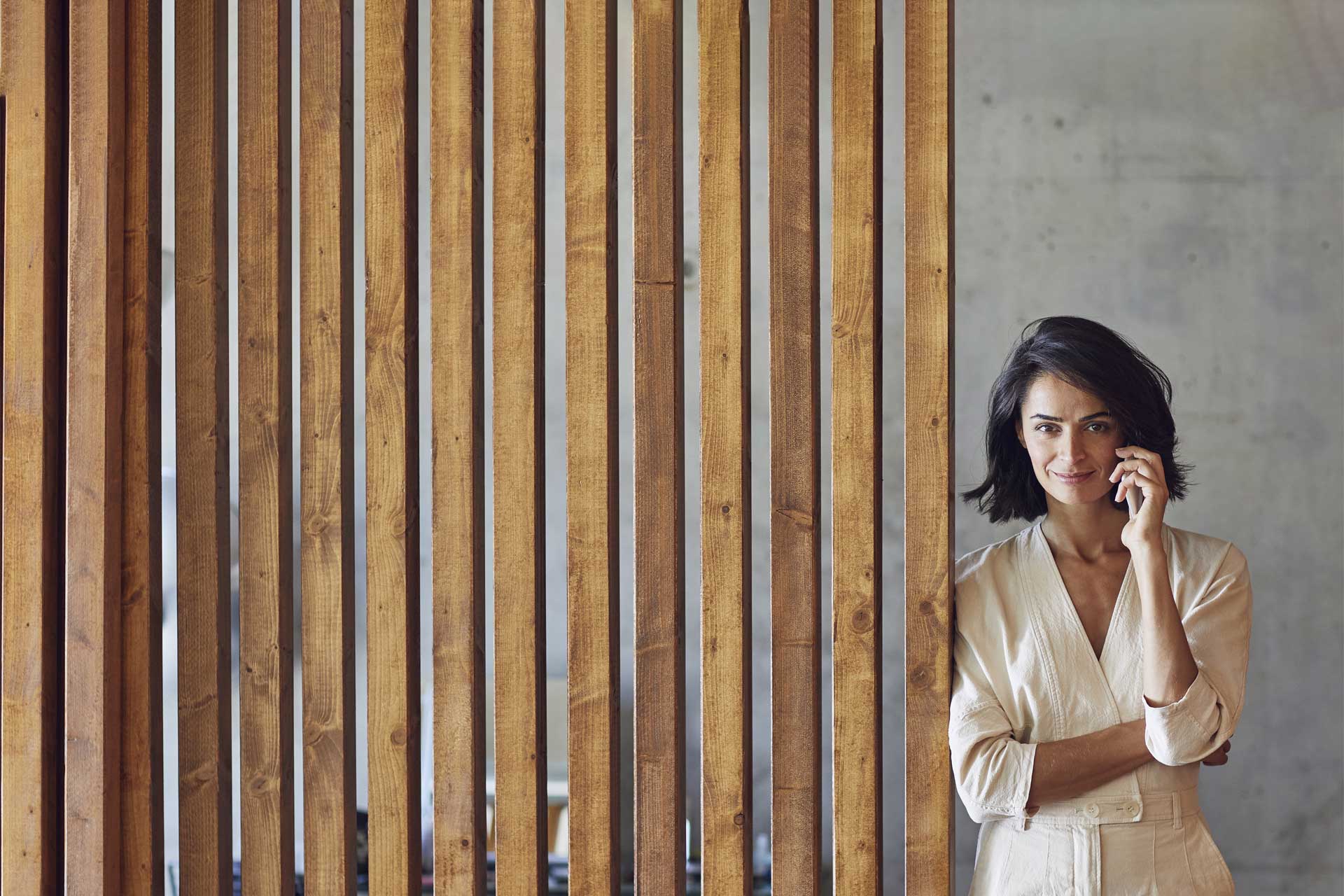 Una donna d'affari dai capelli scuri si trova davanti a una parete di legno e sorride alla fotocamera