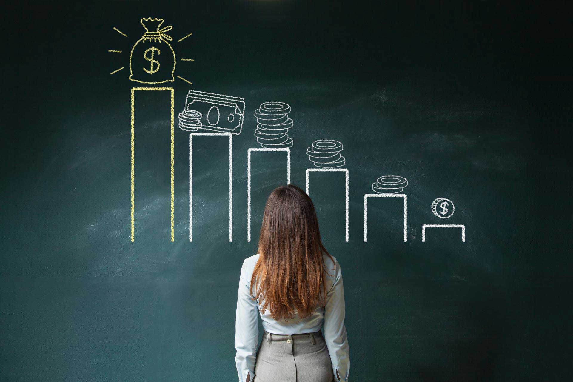 A woman stands in front of a blackboard with financial symbols painted on it