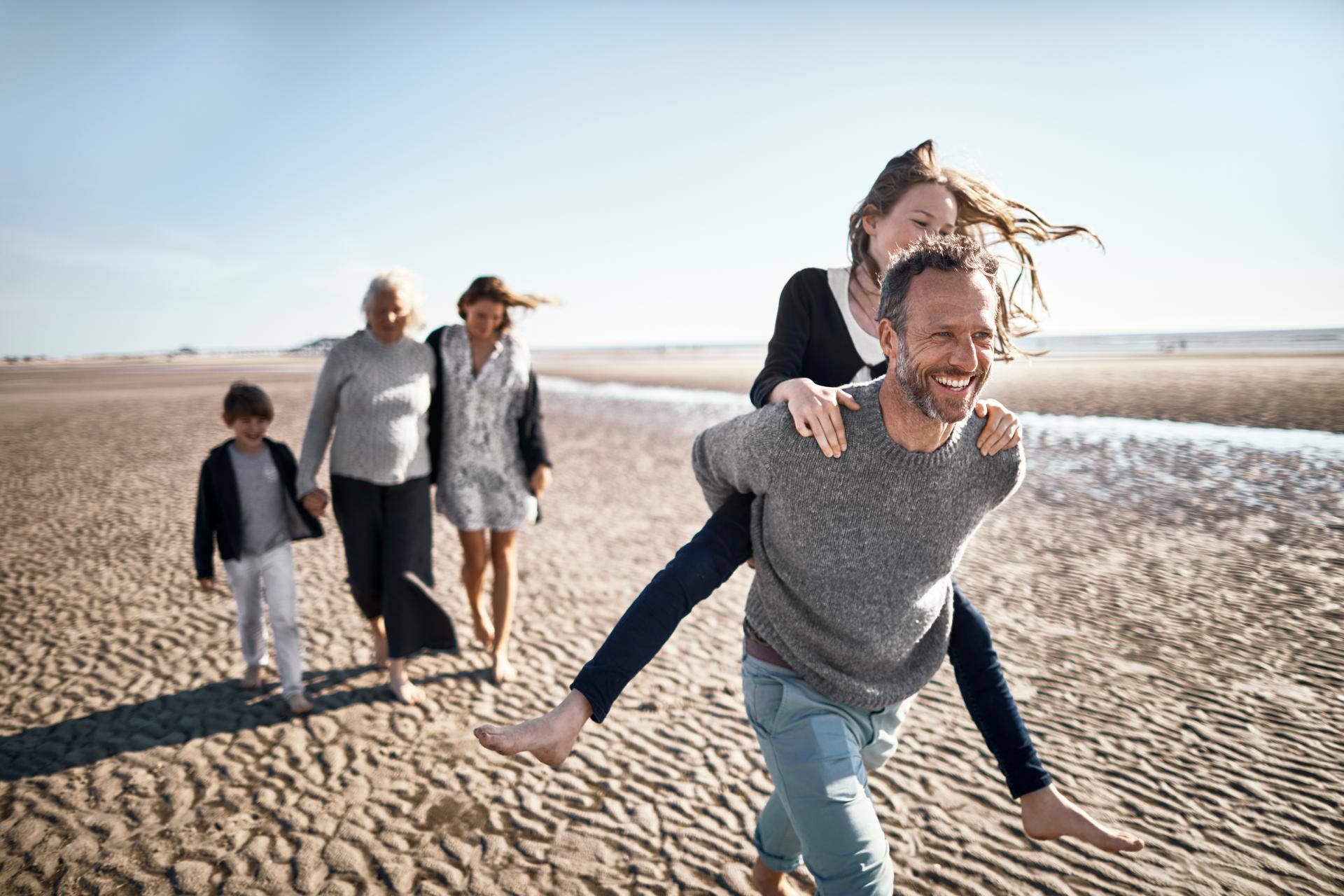 Father plays with daughter and carries her on his back. The family can be seen in the background. The image symbolizes Vontobel's life insurance service.