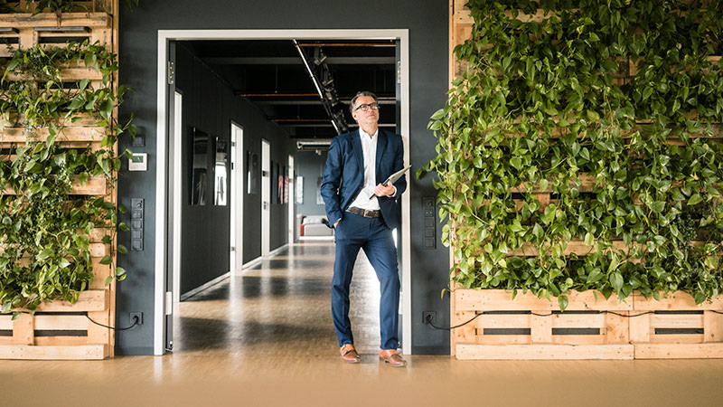 A businessman stands in office spaces with plants on the walls.
